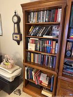 Full view of the wooden bookshelf with shelves filled with books and some papers on the lower shelf, showcasing its height and storage capacity.