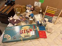 Photo showing the entire lot with multiple stuffed animals, Risk game box, wooden abacus, and small game parts scattered on a bed.