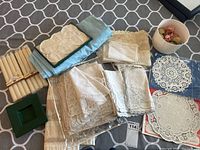 Overview photo showing linens, doilies, napkin rings, candles, and green candle holder arranged together on table.