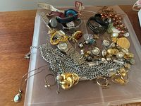 Top view of various jewelry pieces spread out on a wooden surface including multiple watches, metal chain necklaces, earrings, rings, and brooches.