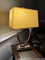 Bronze and marble lamp with curved double-arm base and cream rectangular shade on wooden table near staircase