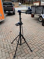 Photo of an adjustable black metal bicycle repair stand with tripod base, blue adjustment knobs, and clamp mount for holding a bicycle frame securely during repairs or maintenance.