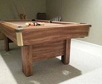 Woodgrain-finished pool table frame and leg with tan felt, balls racked at center