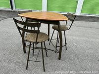 Photo showing triangular wooden table top and three matching metal frame chairs with patterned seats from above.