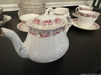 Front-side view of the white bone china teapot with pink rose floral garland and embossed detail