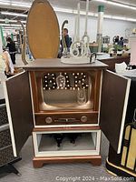 Full front view of the cabinet showing open upper doors with lighted 'BAR' sign inside, wine glass holders, and the open lower shelf with wine bottles.