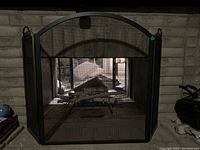 Heavy metal fire screen placed in front of a fireplace showing its full structure and arched top with two side panels.