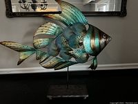 Front view of the metal fish sculpture showing color, dimensions, and stand.