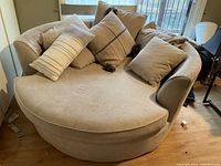 Image of a large beige cuddle couch with several cushions placed on it, showing the shape, color, and condition of the couch.