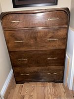 Front view of mid-century modern dresser showing wood grain and four drawers with brass handles.