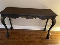 Photo of a rectangular solid oak console table stained espresso with bronze accent carvings on front apron and curved legs ending in claw feet.