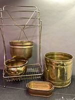 Photo showing brass towel rack with chain and three brass containers of varying sizes including a medium bowl, a larger cylindrical container, and a small oval container.