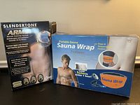 Photo of Slendertone Arms Muscle Training System box and Portable Sauna Wrap box side by side showing packaging and branding.