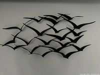 Photo showing a black metal wall art sculpture of multiple birds flying together in a dynamic arrangement on a white wall.