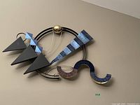 Abstract geometric metal wall art with blue and complementary colors, circular and triangular shapes, mounted on a white wall.