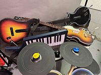 Xbox Guitar Hero full band set showing four guitar controllers, keyboard controller, and drum pads with cymbals and drumsticks arranged on a stand.