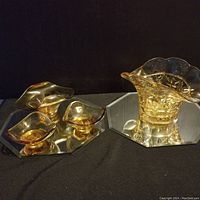 Five pieces of amber glassware displayed on two hexagonal mirrored trays, including a large scalloped-edge vase and three smaller dishes.