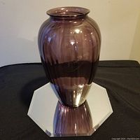 Full view of the amethyst purple glass vase showing its shape, texture, and color on a reflective surface.
