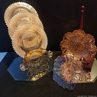 Lot of vintage pink depression glass items including diamond pattern plates, a flower-shaped serving plate, scalloped bowl with handles, and tall handled cutting board.