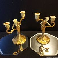 Pair of Art Nouveau style candelabras with female figurines and two candle holders each, shown on reflective surfaces