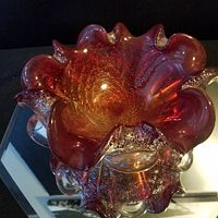 Top angled view showing the ruffled edge, red and amber colors, and gold fleck pattern on the glass dish.