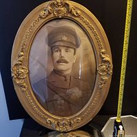 Full view of antique oval bubble glass frame with ornate gold finish and vintage military portrait inside