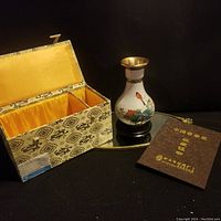 Photo showing the cloisonné vase next to open silk-lined box and certificate booklet