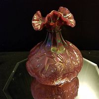 Full view of the iridescent ruffled top and embossed designs on the body of the vase reflecting green and gold hues under light.