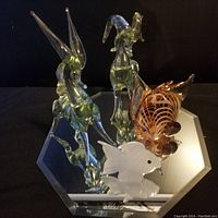 Front angled view of four hand blown glass animal figurines on mirrored surface, showing insect, horse, and two fish.