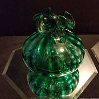 Front and angled view of green glass vase on mirrored surface showing shape, design, and color details.
