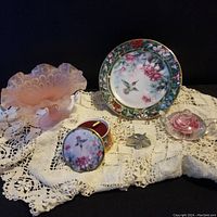 Overall lot with hummingbird music box, decorative plate, pink frosted glass rose trinket container, bowl, and metal star on lace cloth