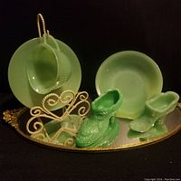 Front view of jadeite lot including glass plates, teacup, and two shoe figurines on mirrored base.