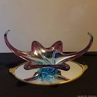 Full front view of the colored glass centerpiece bowl on the oval mirrored tray on a dark surface with a neutral background.