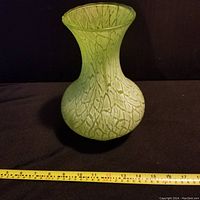 Front view of the vintage green glass vase with white speckled pattern with measuring tape showing width approximately 7 inches.