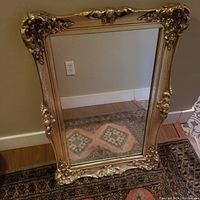 Full view of ornate vintage wall mirror with gold decorative frame featuring floral and scroll details.