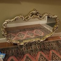 Full view of the vintage ornate wall mirror showing carved scrollwork frame with gold and cream distressed finish.