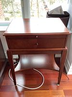 Front view of the wooden Bombay end table showing top surface, drawer and lower shelf with tapered legs.