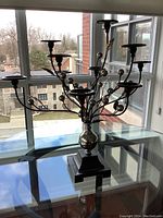 Photo showing the full front view of the metal candelabra on a glass table with city view background.