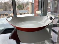 Side view of orange enameled cast iron pan showing curved shape and handles