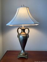 Front view of lamp with light on showing white fabric shade and metal base with handles