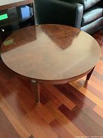 Front angle view of the round wooden coffee table showing the polished surface and one leg with a brass tip and medallion.