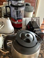 Lot items including red KitchenAid food processor, white hand mixer, black and white electric coffee grinder, and stainless steel electric kettle on granite countertop.
