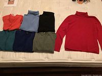 Seven cashmere sweaters and turtlenecks in various colours arranged on a bed, showing condition and colours.