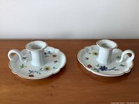 Pair of white Limoges porcelain candleholders with multicolored floral motifs and gold edging displayed on wooden surface