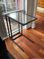 C table placed near window on wooden floor, showing side profile and frame design.