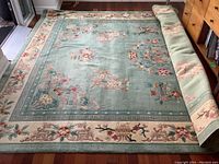 Full view of the green oriental wool area rug approximately 9 x 12 feet laid on floor, showing overall design and some rolled portion.