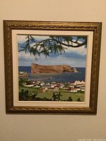 Front view of the signed framed landscape painting depicting coastal village and rock formation in background.