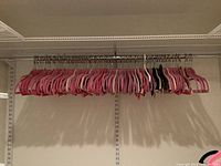 Wide view showing over 100 pink velvet hangers and some black and white hangers hanging on a closet rod.