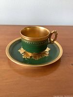 Photo showing side view of green and gold Limoges teacup on matching saucer with detailed gold trim and leaf designs