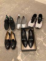 Overview of five pairs of women's shoes including sneakers, flats, loafers, and pumps on carpeted floor.